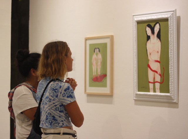 Members of the public engage with paintings by Citra Sasmita during the opening of "Tanda Seru" at Uma Seminyak - Image courtesy of Futuwonder